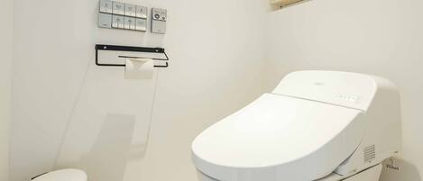 A modern bathroom with a white toilet, a trash bin, and a wall-mounted control panel.