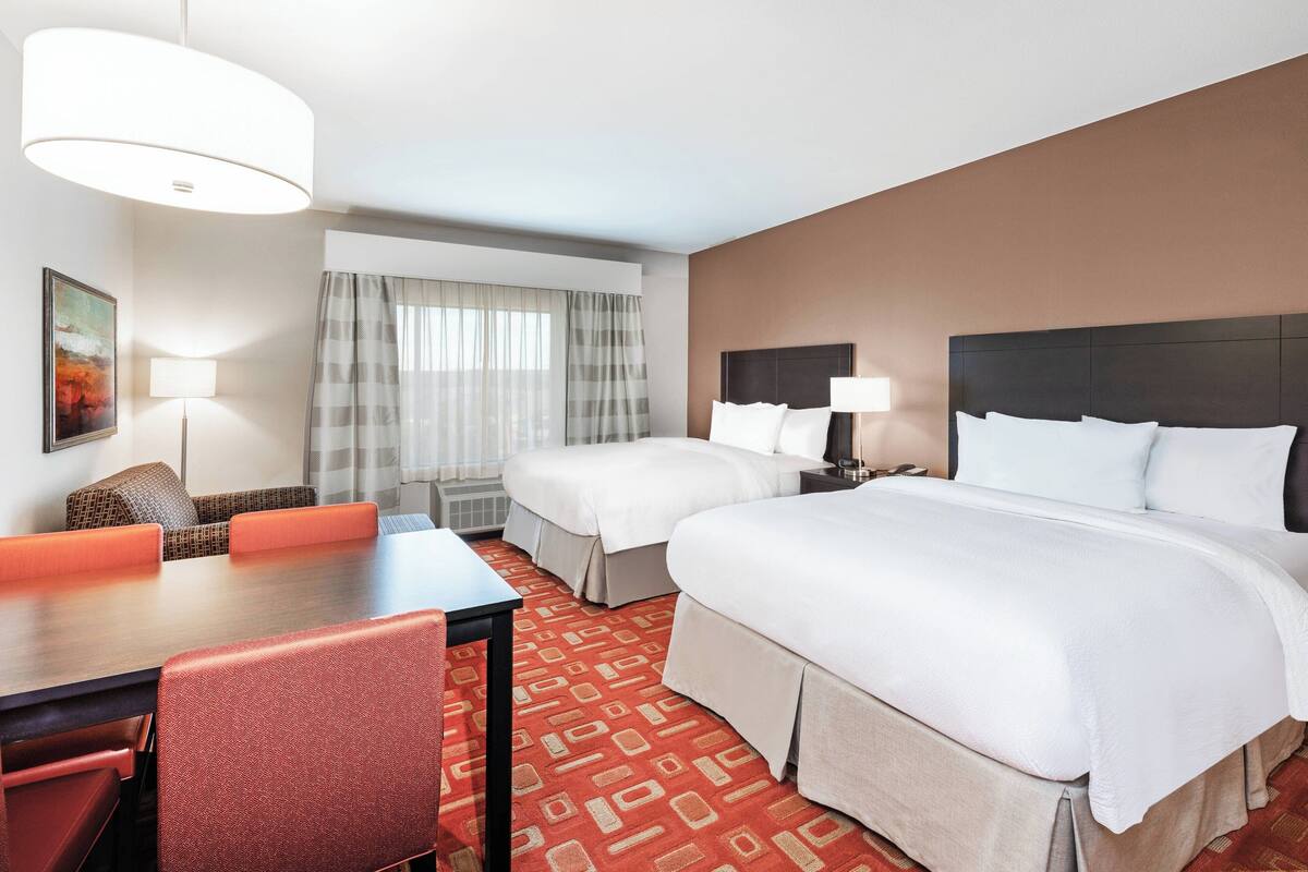 Ein Hotelzimmer mit zwei Betten, einem Esstisch und einer Couch.