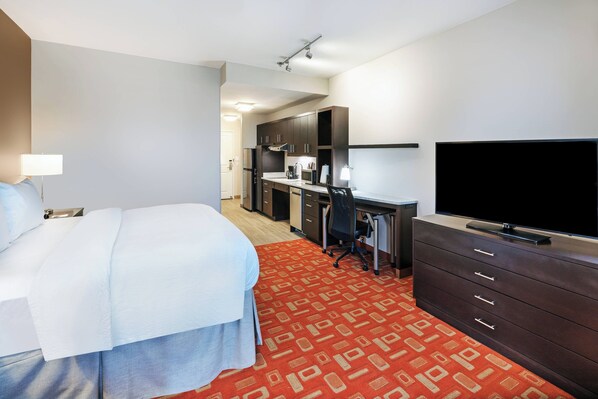 A hotel room with a bed, desk, television, and kitchenette.