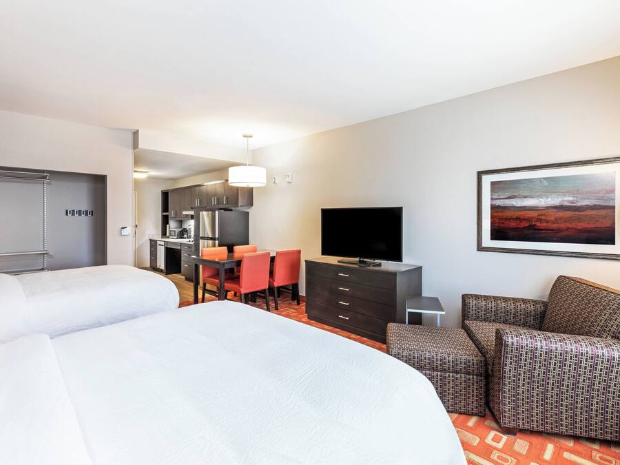 A hotel room with two beds, a dining area, a TV, and a painting on the wall.