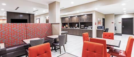 A modern restaurant with high tables and orange chairs, a counter with a menu, and a TV mounted on the wall.