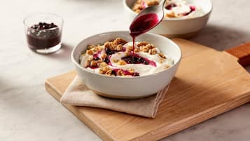 Un tazón de yogur con granola y bayas sobre una tabla de madera.