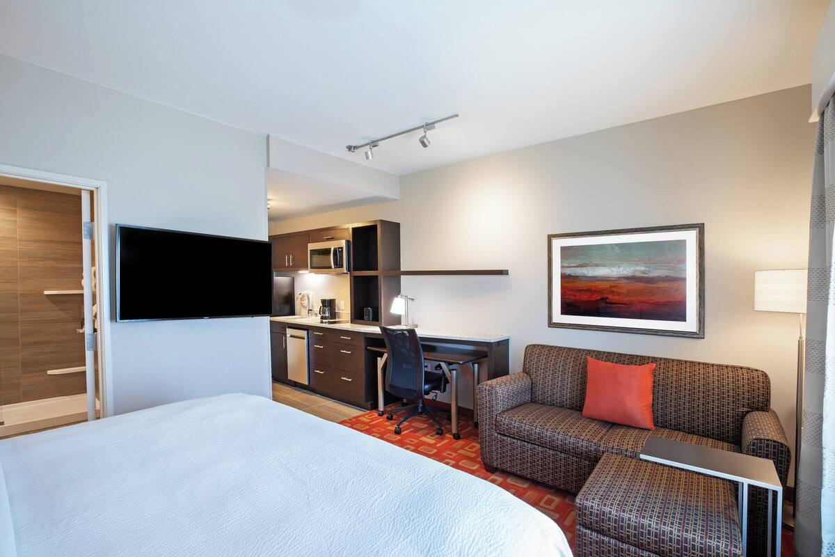 Ein Hotelzimmer mit Bett, Schreibtisch, Sofa, Fernseher und einem Gemälde an der Wand.