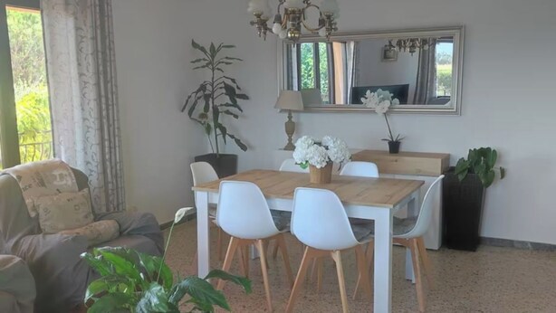 A dining area with a wooden table and white chairs, a chandelier, and a large mirror above the table. - Mas Turró - Castelló d'Empúries (Castellón de Ampurias)
