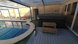 An indoor swimming pool with a hot tub, a small wooden table, and a bench. - Mas Turró - Castelló d'Empúries (Castellón de Ampurias)