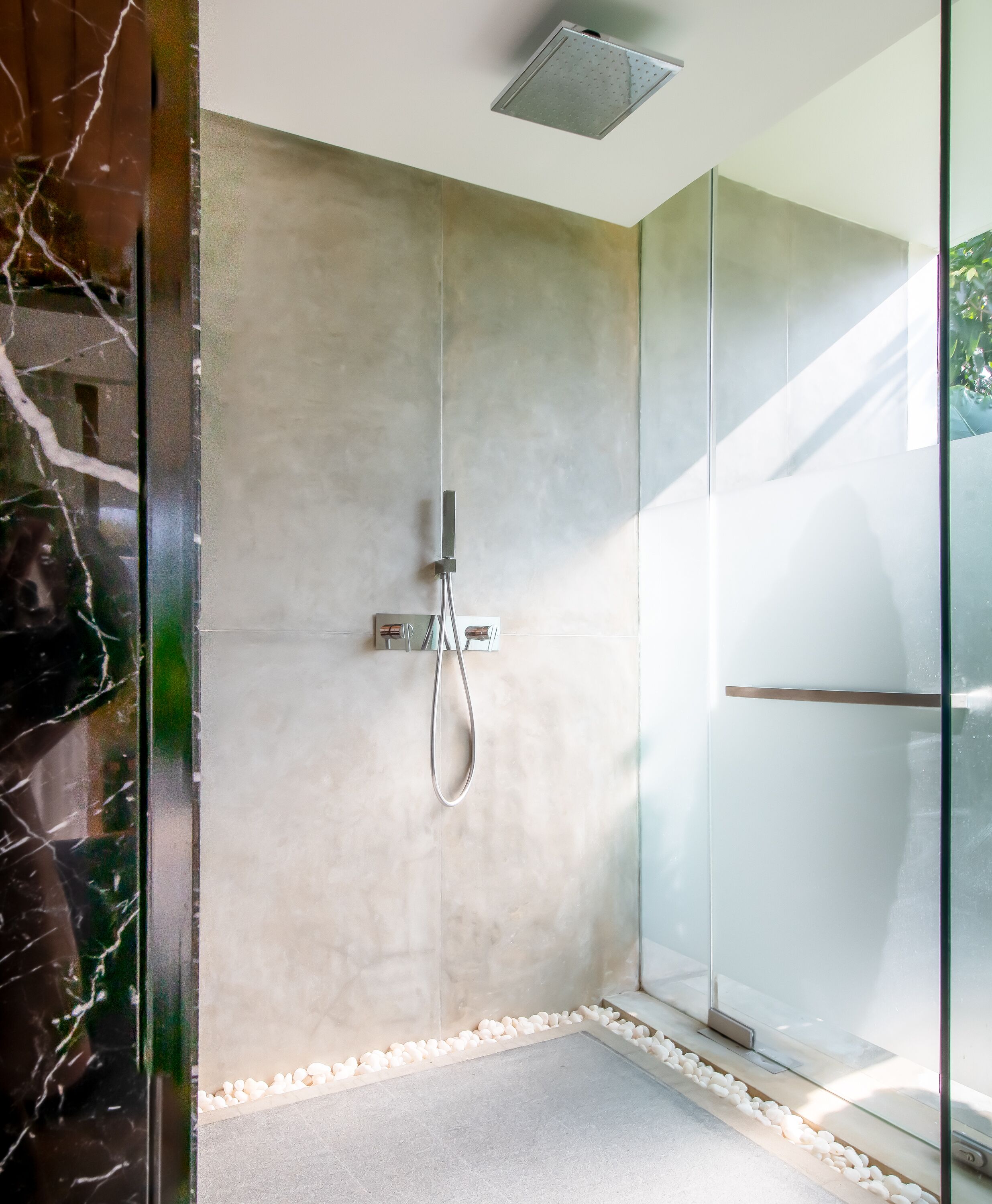 Een moderne douche met een glazen cabine, een accentmuur van marmer en een rand van kiezelstenen.