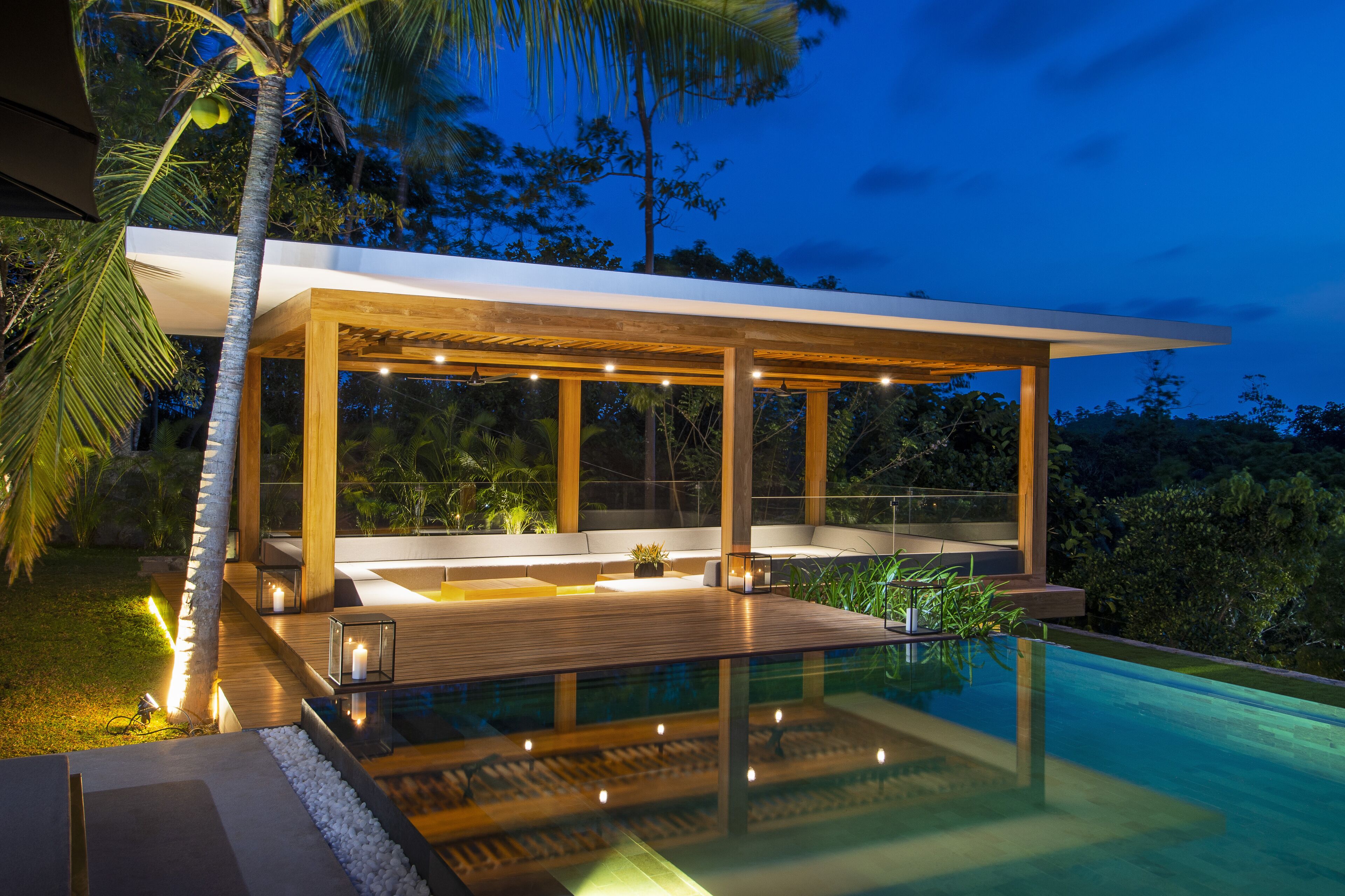 Un área de piscina moderna al aire libre con cubierta de madera, asientos e iluminación ambiental.