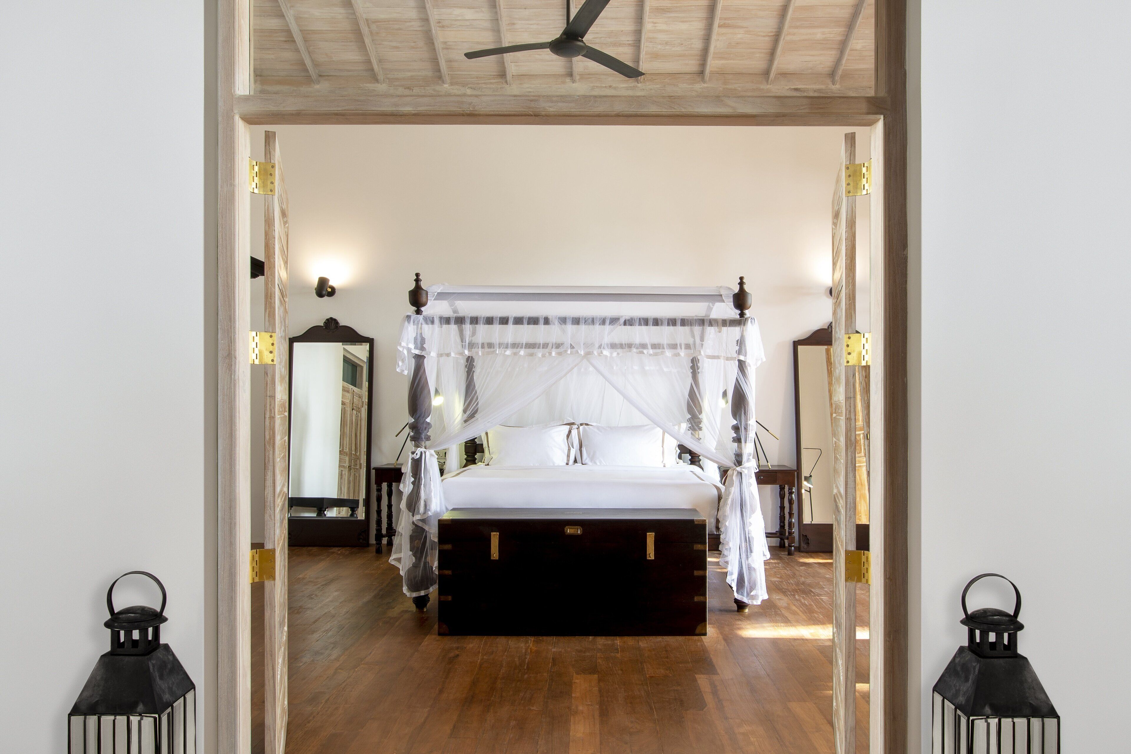 Ein Schlafzimmer mit Himmelbett, Holzboden und Deckenventilator.
