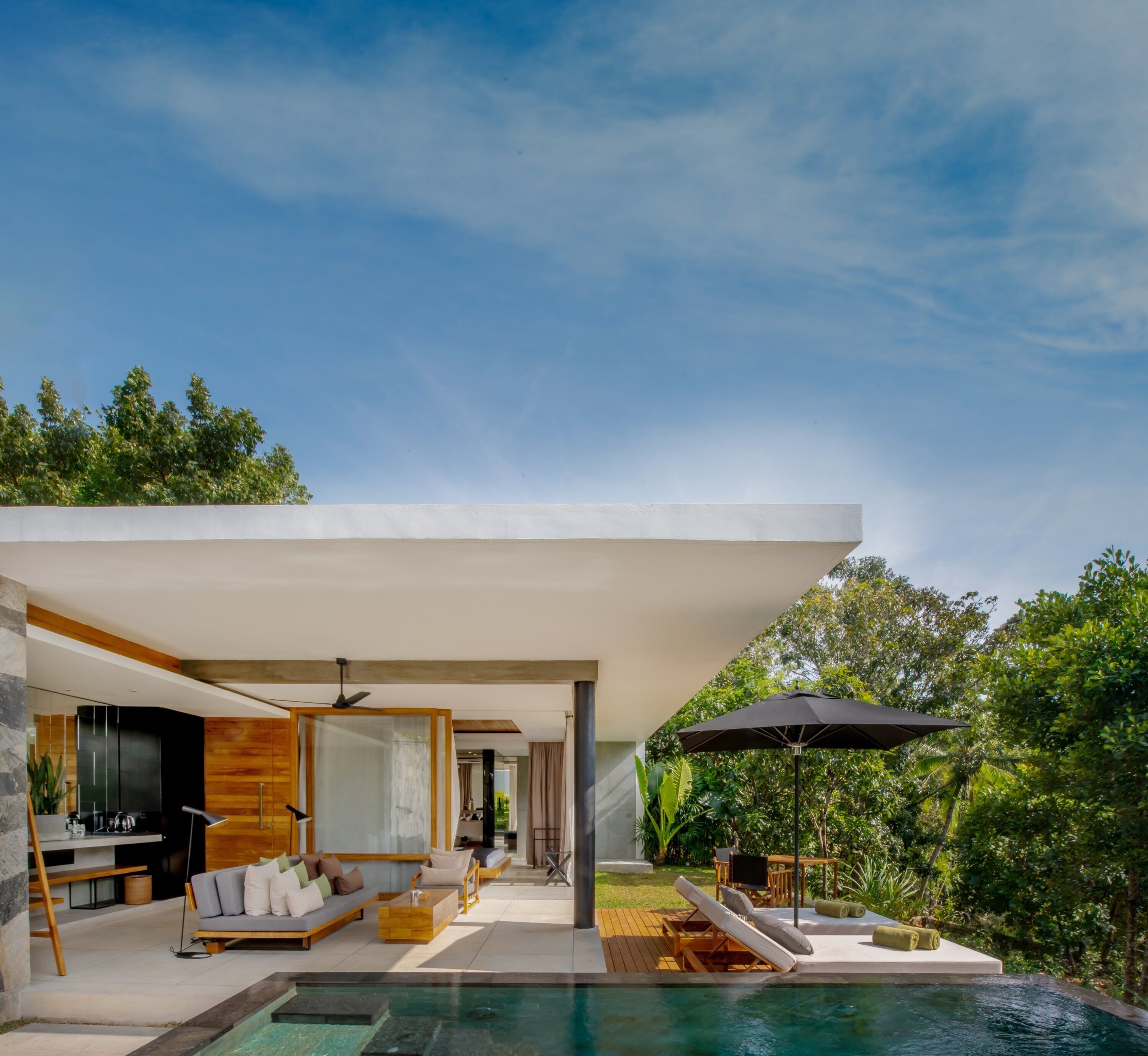 A modern house with a pool, outdoor seating, and a large umbrella.