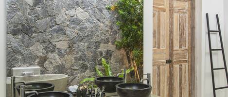 Un baño con pared de piedra, dos lavamanos negros tipo lavabo, una bañera y una puerta de madera.