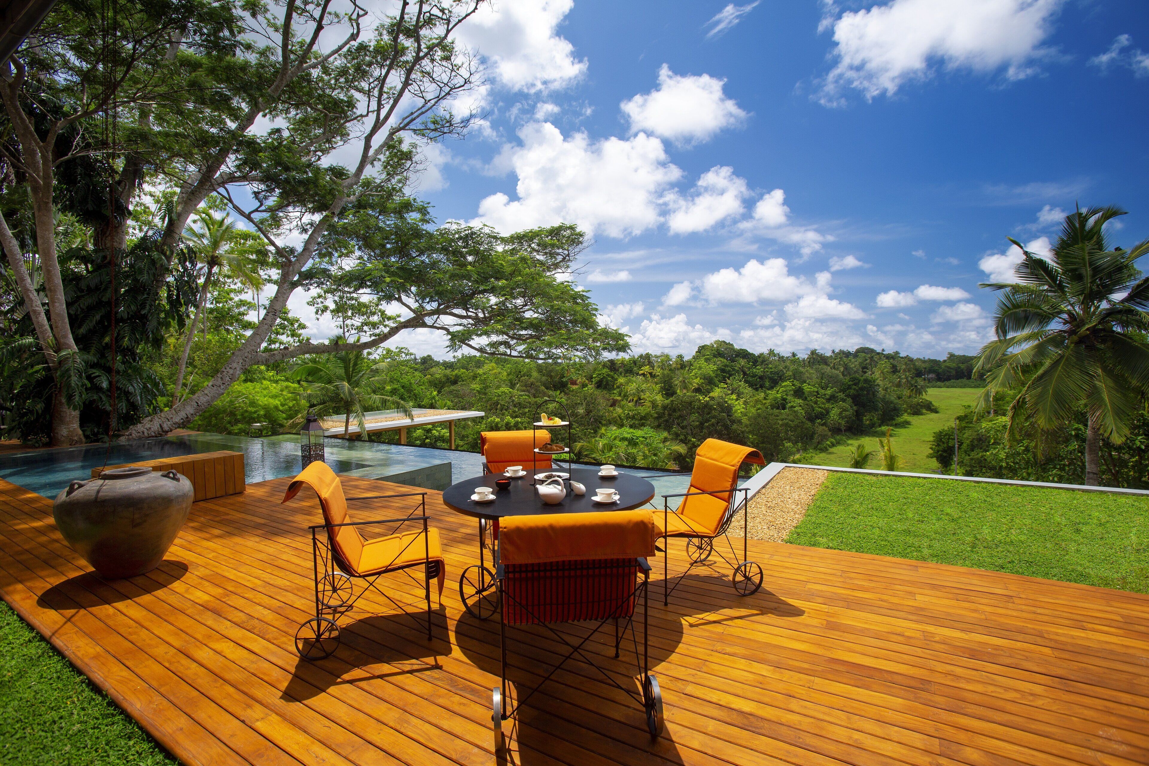Un área de comedor al aire libre con mesa y sillas, con vista a una piscina y abundante vegetación.