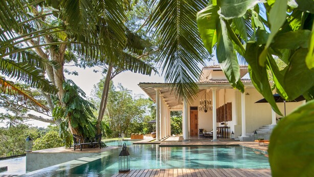 An infinity pool with wooden decking, surrounded by lush greenery and palm trees. - Haritha Villas & Spa (Hikkaduwa)