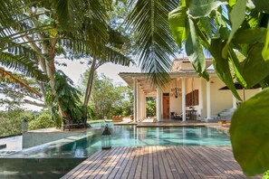 An infinity pool with wooden decking, surrounded by lush greenery and palm trees. - Haritha Villas & Spa (Hikkaduwa)