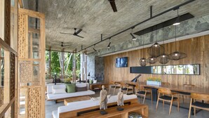 A modern living room with a wooden dining area, built-in shelves, and a large TV on the wall. - Haritha Villas & Spa (Hikkaduwa)