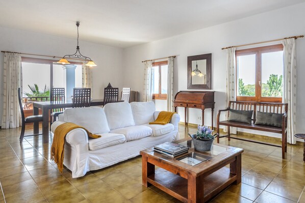 A spacious living room with a white sofa, wooden coffee table, and a dining area with a table and chairs.