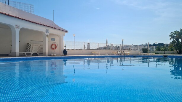 En swimmingpool med fliseark kant, en redningskrans og et hegn.