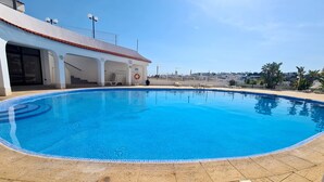 En udendørs swimmingpool med krystalklart blåt vand, en flisekant og udsigt til en by i baggrunden.