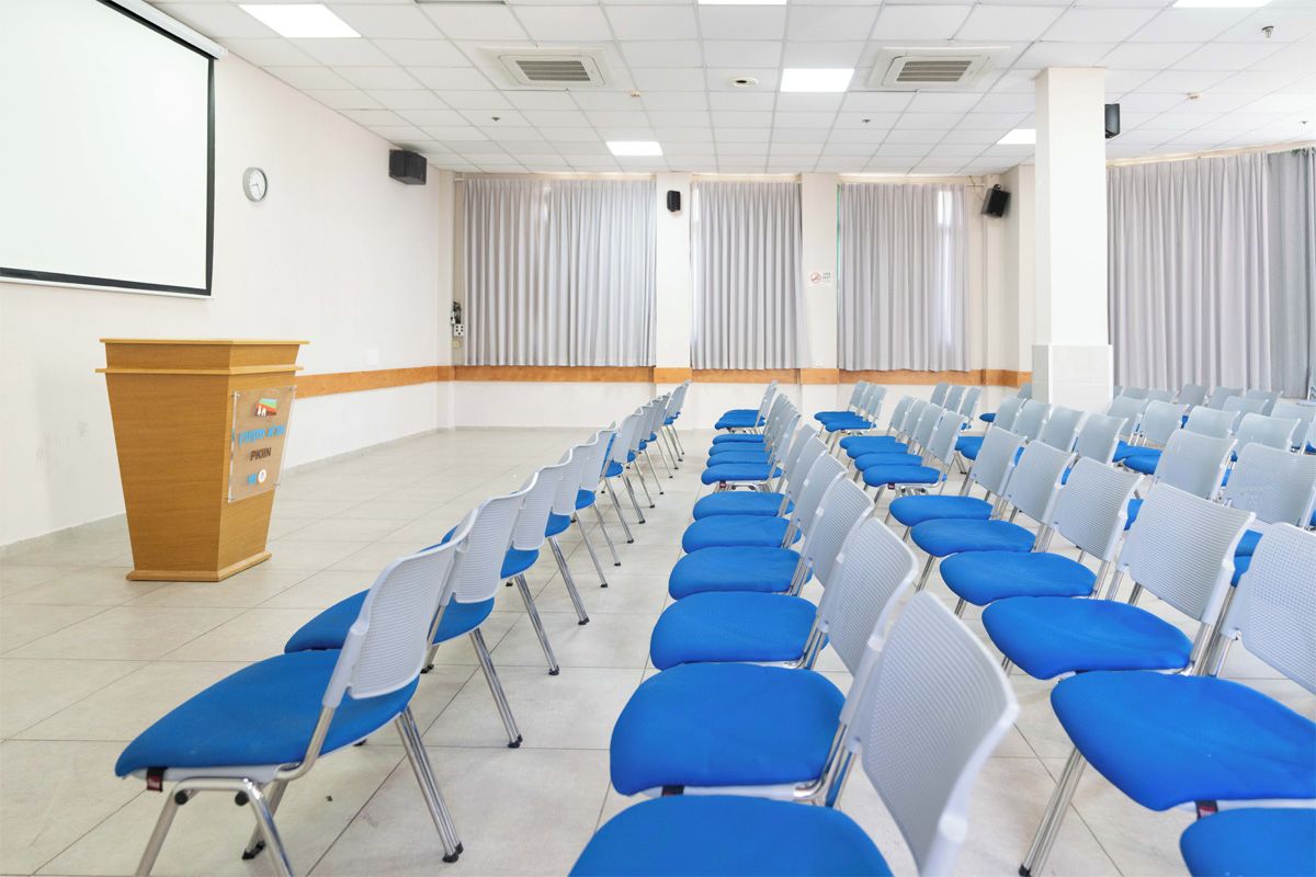 Ein Konferenzraum mit Reihen von Stühlen, einem Rednerpult und einer Projektionsleinwand.