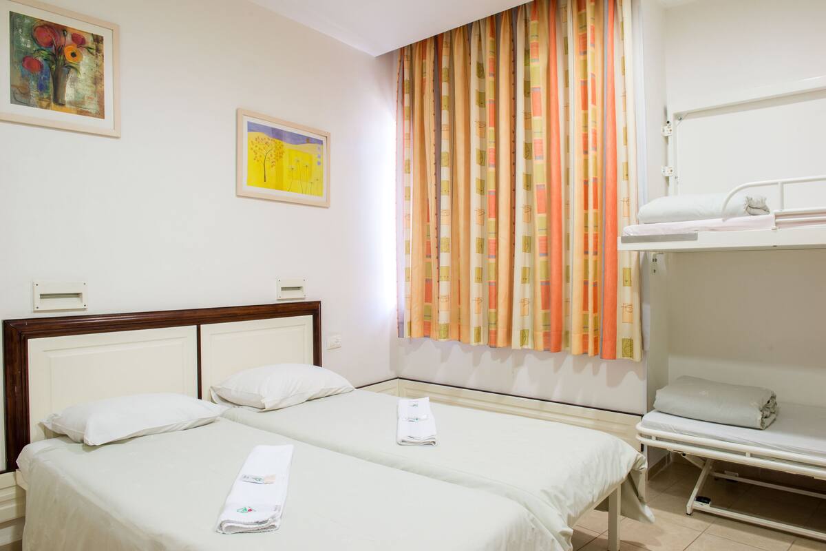 A hotel room with two beds, a window with striped curtains, and artwork on the walls.
