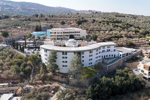 A multi-story hotel with a curved facade, surrounded by trees and hills. - HI Pkiin Hostel (Peki'in)
