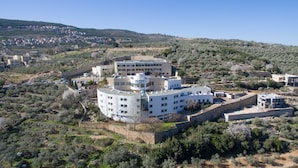 A multi-story building with a central courtyard, surrounded by olive trees and a stone wall. - HI Pkiin Hostel (Peki'in)