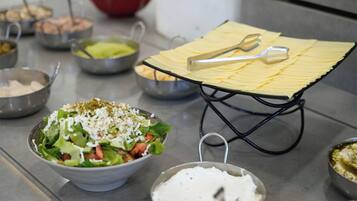 Una cuina amb un taulell on hi ha diversos aliments i utensilis, incloent un bol de amanida, una safata de pa pla i diversos bols amb diferents ingredients.