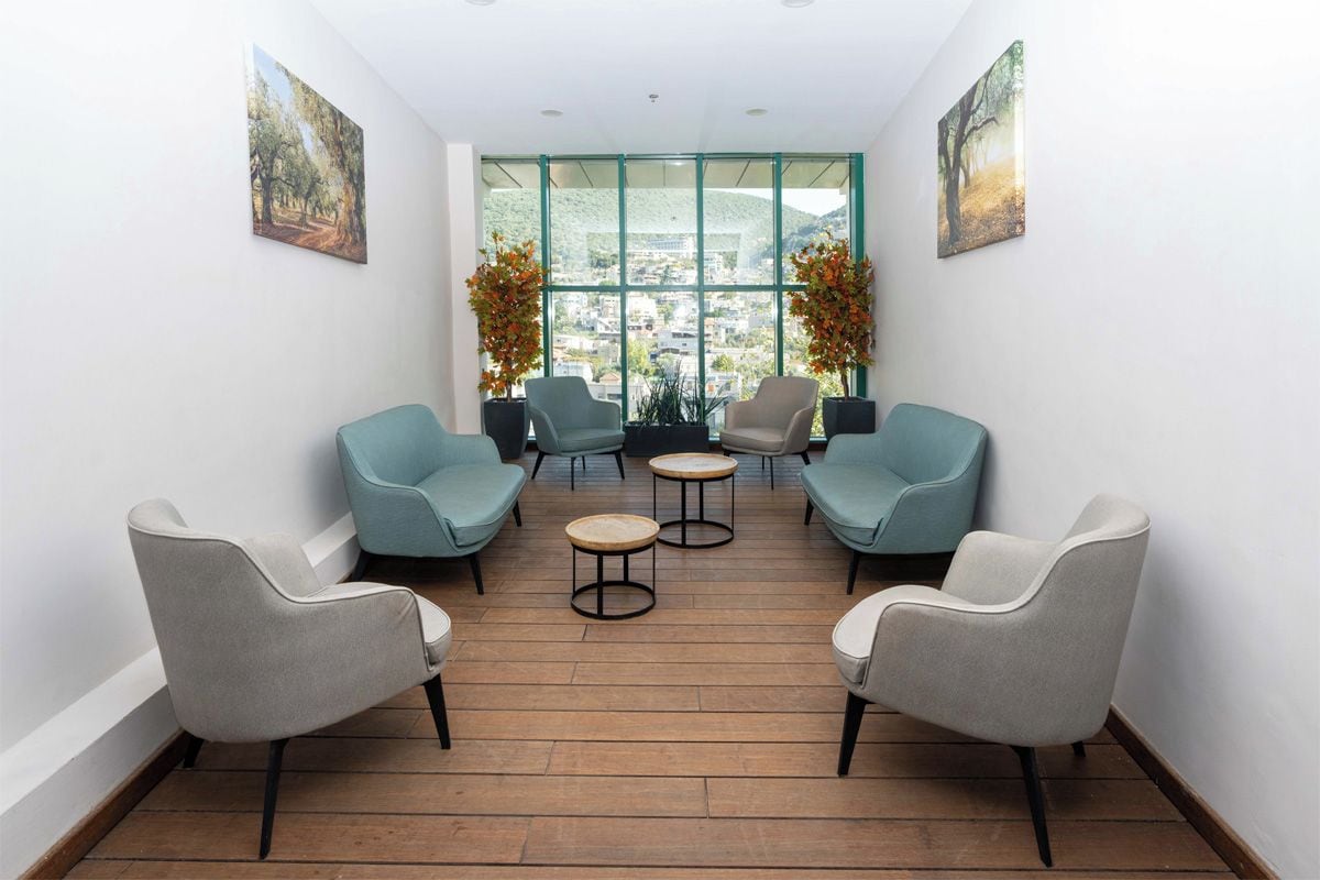 A room with a wooden floor, four chairs, two small round tables, and large windows with a view of a cityscape.