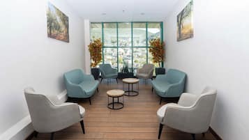 A room with a wooden floor, four chairs, two small round tables, and large windows with a view of a cityscape.