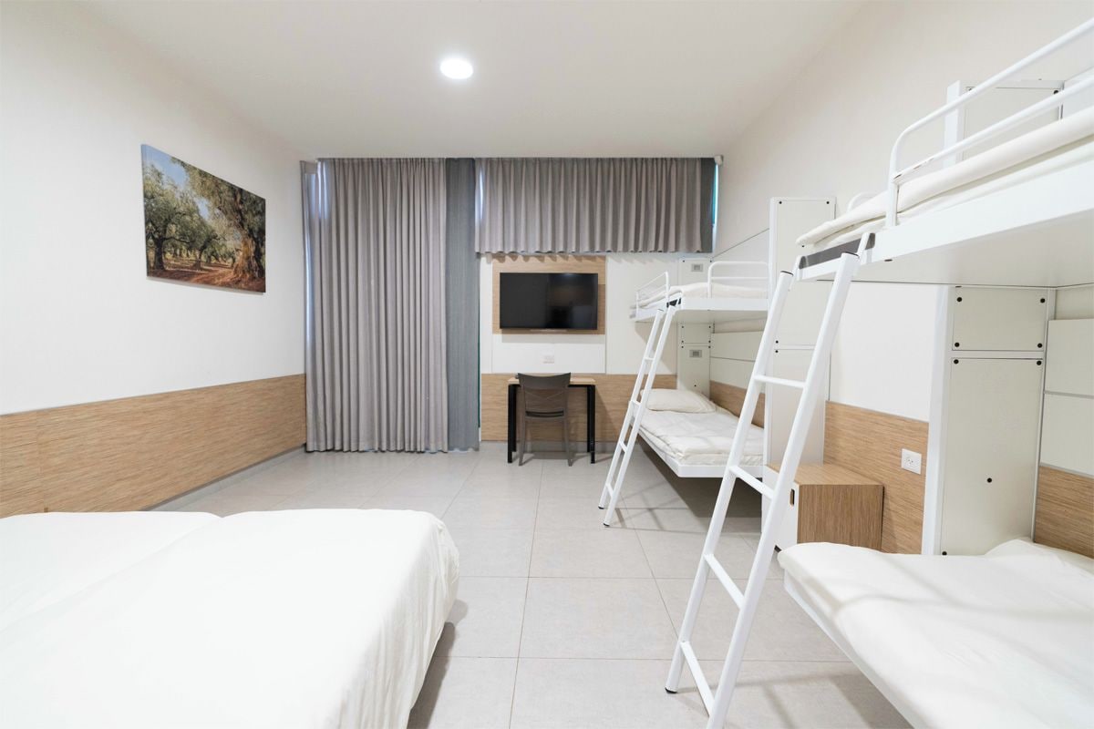 A hotel room with bunk beds, a desk, a chair, a television, and a painting on the wall.