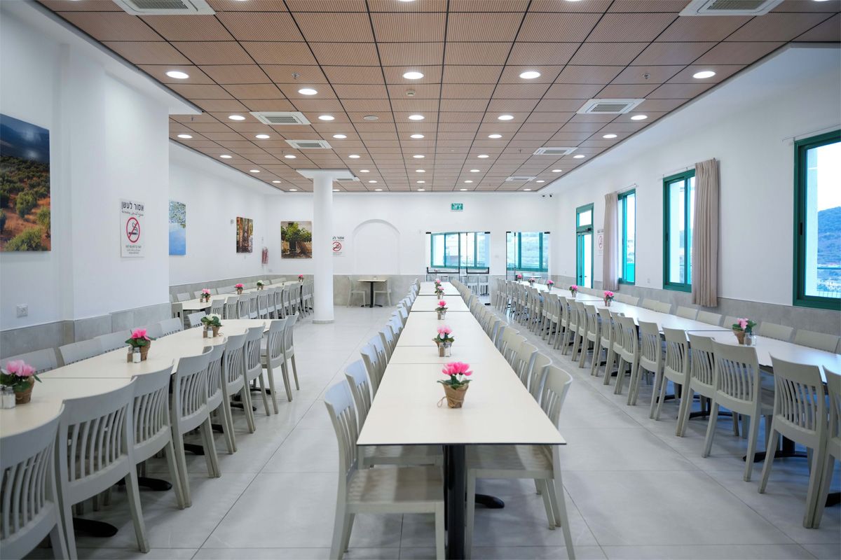 A spacious dining area with long tables and chairs, large windows, and artwork on the walls.