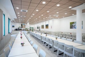 A spacious dining area with long tables and chairs, ceiling lights, and wall-mounted artwork. - HI Pkiin Hostel (Peki'in)