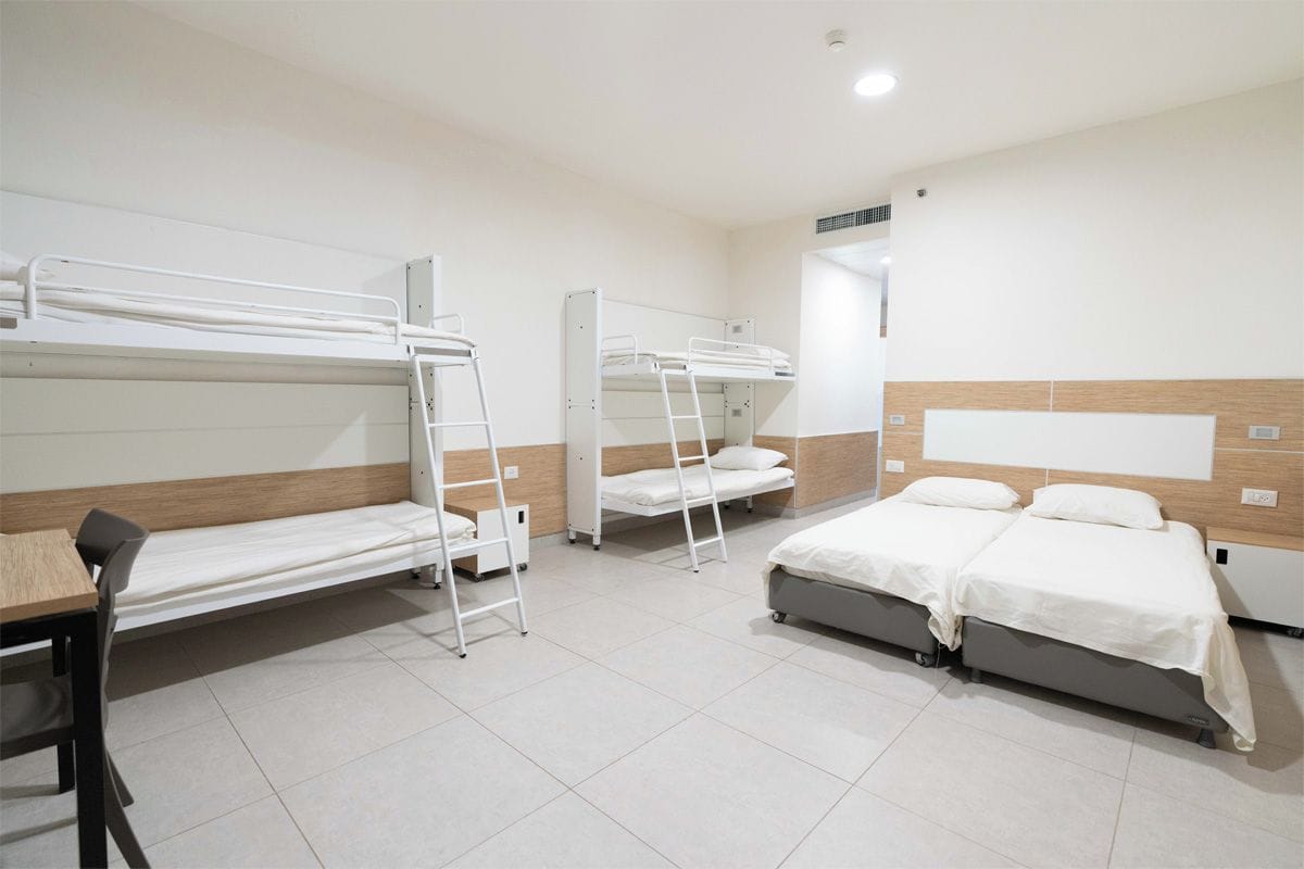 A dormitory room with bunk beds, a desk, and a chair.