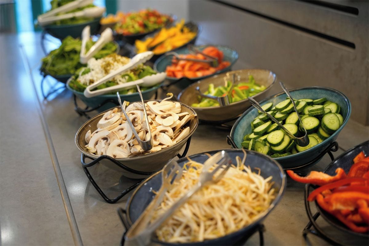 A buffet with various food options including mushrooms, cucumbers, and shredded cheese.
