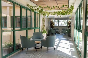 A modern interior with large windows, green-framed glass doors, and a seating area with chairs and a small table. - HI Pkiin Hostel (Peki'in)