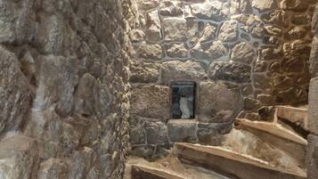 A stone staircase in a narrow, dimly lit corridor with rough stone walls and a small window at the top.