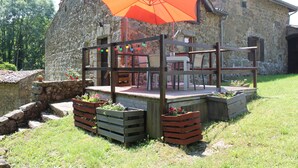A rustic stone building with a wooden deck and an orange umbrella. - Le Bouchon de Campagne (Saint-Barthelemy-Grozon)