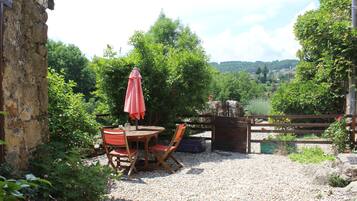 A rustic outdoor seating area with a table and chairs, surrounded by greenery and a gravel path.