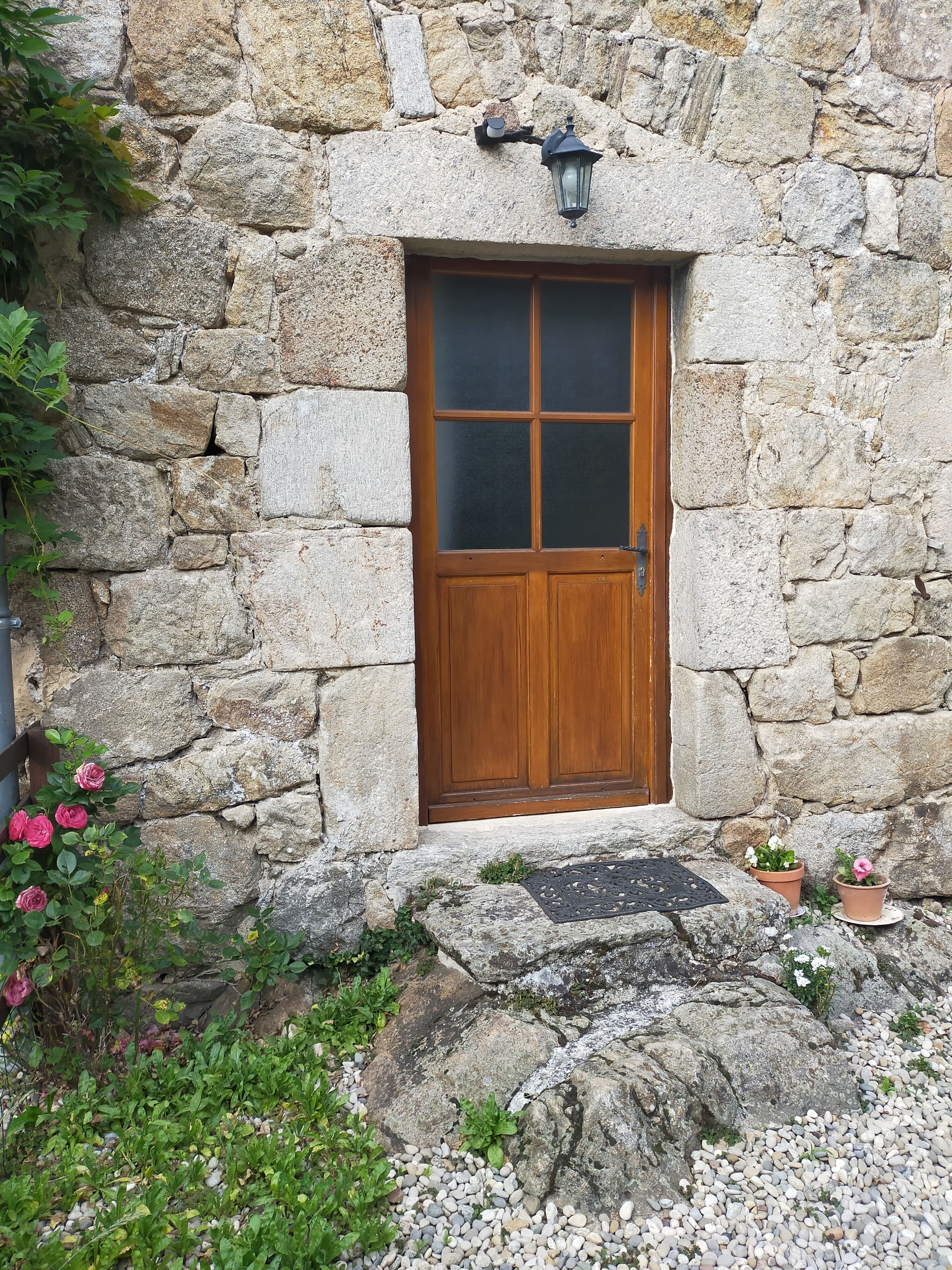 A stone building with a wooden door, a lantern above the door, and potted plants around the entrance.