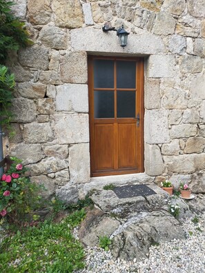 A stone building with a wooden door, a lantern above the door, and potted plants around the entrance. - Le Bouchon de Campagne (Saint-Barthelemy-Grozon)