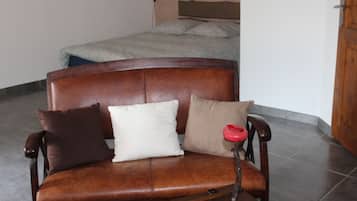 Een bruine leren bank met drie kussens in een ruimte met betegelde vloer en een houten deur.