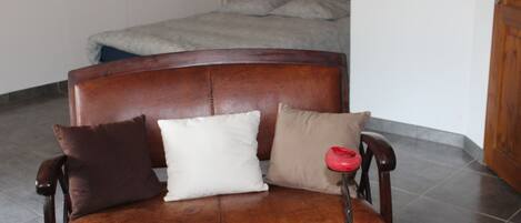 Un sofá de cuero marrón con tres almohadones en una habitación con suelo de baldosas y una puerta de madera.