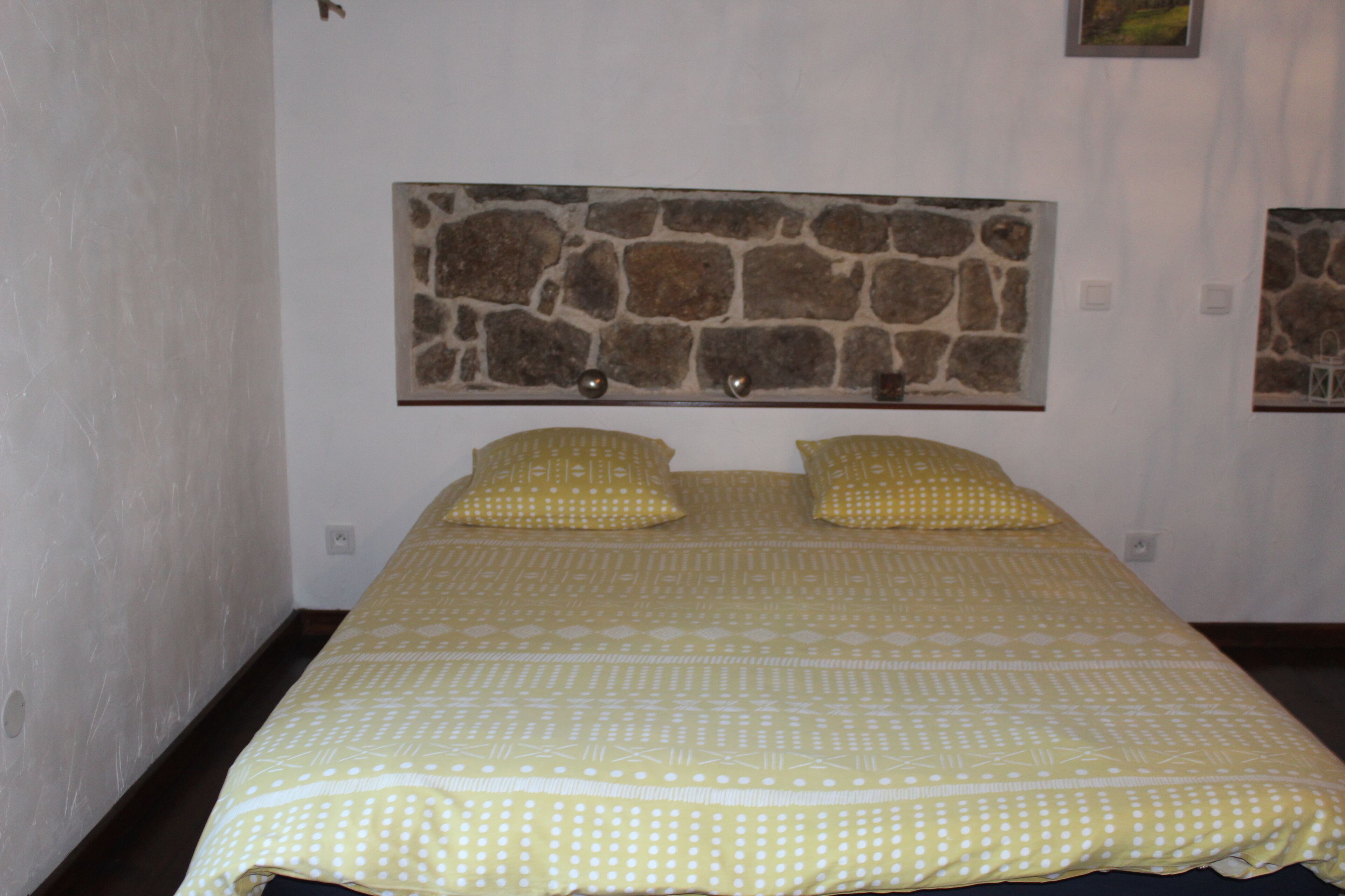 Camera da letto con un letto, due cuscini, una testiera effetto pietra e una parete semplice.