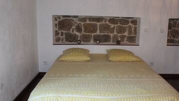 Camera da letto con un letto, due cuscini, una testiera effetto pietra e una parete semplice.