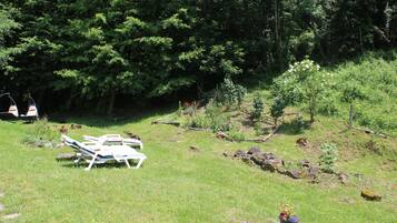 A grassy area with white lounge chairs and a small garden with rocks and plants.