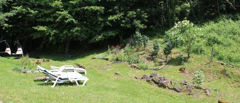 A grassy area with white lounge chairs and a small garden with rocks and plants.