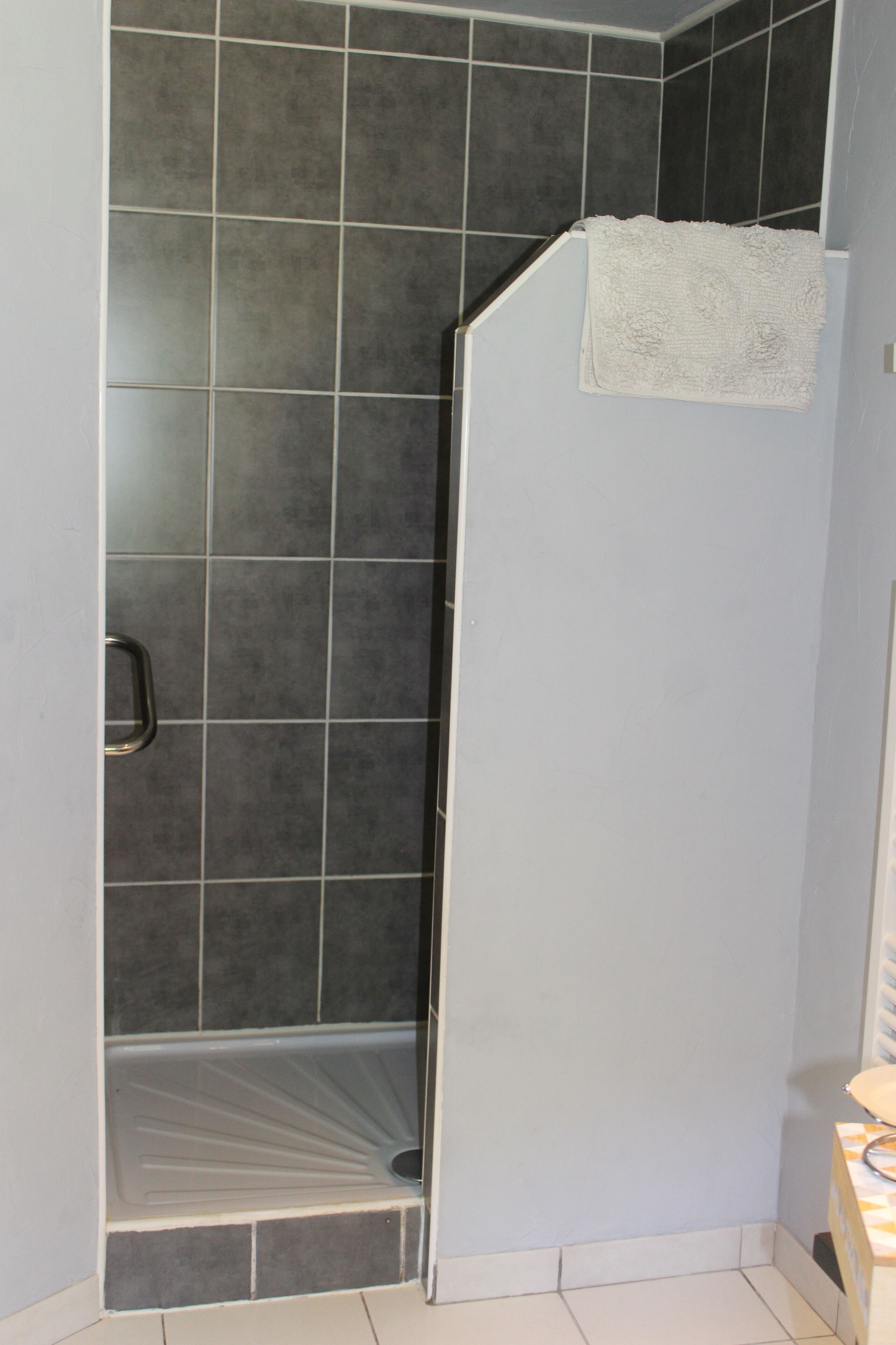 Un baño con baldosas oscuras, una toalla blanca colgada en la pared y una puerta de ducha.