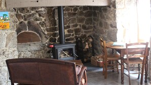 A stone fireplace with a wood-burning stove, a wooden bench, and a dining table with chairs in a rustic room. - Le Bouchon de Campagne (Saint-Barthelemy-Grozon)