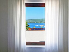 A window with white curtains, a view of a marina with boats, and a hilly landscape in the distance. - Apartment 2 - two double rooms sea view terrace (apartment 2) (Punat)