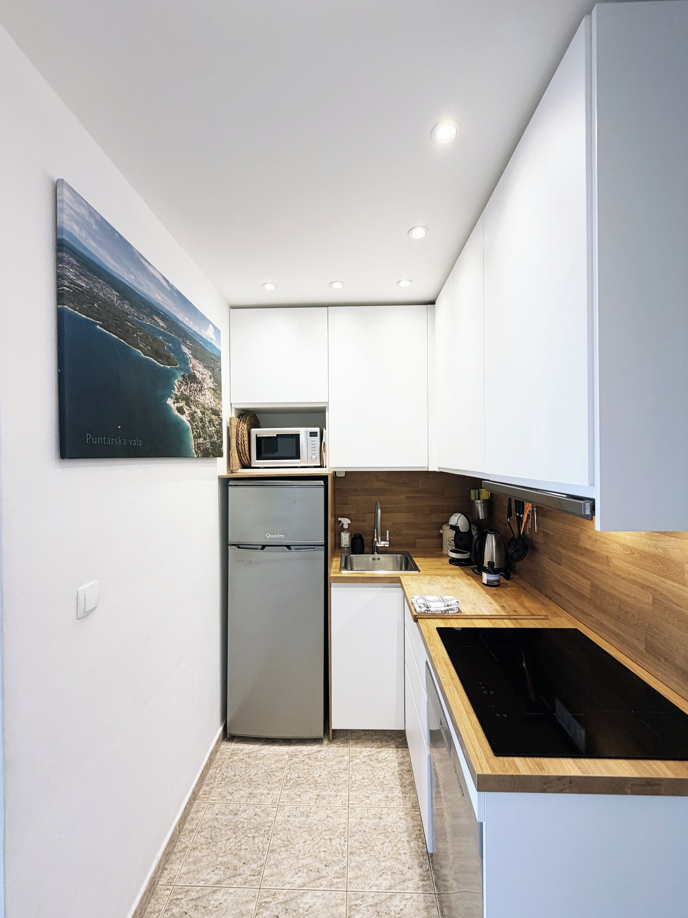 Een moderne keuken met witte kasten, een roestvrijstalen koelkast, een magnetron en een houten aanrecht.