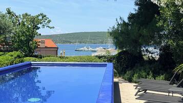 A clear blue swimming pool with lounge chairs and a view of the sea and boats.